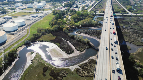 Elevated roadway spans expansive marshlands bordering major industrial zones river channels. Busy traffic flow connects regional freight hubs across maritime vistas within North Charleston, SC