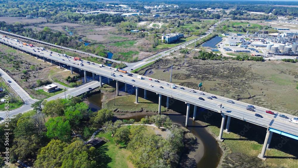 Fototapeta premium Elevated roadway spans expansive marshlands bordering major industrial zones river channels. Busy traffic flow connects regional freight hubs across maritime vistas within North Charleston, SC