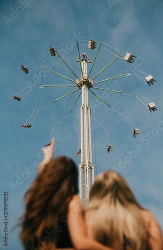 Canvas-taulu Two young women embrace looking up at a thrilling fairground ride