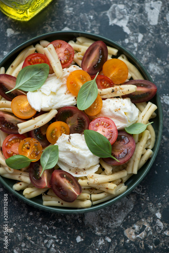Pasta salad with casarecce, mixed tomatoes and torn mozzarella cheese, vertical shot on a dark-brown granite background, middle closeup