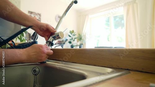 Securing flexible water lines into new kitchen faucet, hand assembling plumbing connections during DIY repair. Installing tap hoses onto mixer fixture above sink, home improvement maintenance process
