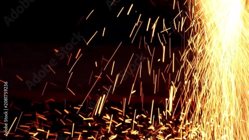 Bright yellow and orange fiery sparks showering down and scattering across a dark surface during an industrial metalworking process.