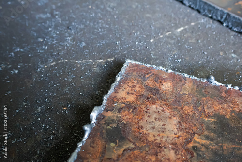 Fotografie A detailed view of a thick steel plate after being cut by a torch or plasma cutter, showing a rough metallic edge surrounded by residual dross and slag