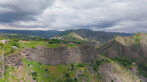Aerial view Garni castle with Azat gorge. A drone shows a high view of a historic site on a hill in Armenia. Green hills surround the area. Clouds cover parts of the sky, creating a nice contrast.