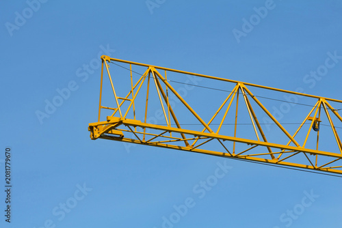 Fotografie A bright yellow construction crane jib stands out clearly against a cloudless blue sky