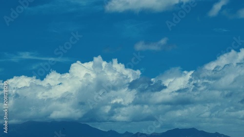 A serene scene of deep blue sky with fluffy cumulus clouds drifting gently towards mountains in the distance
