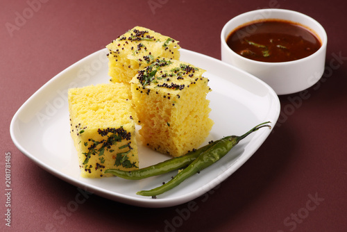 Khaman Dhokla made up of rice chana dal is a popular breakfast or Snacks recipe from Gujarat, India, served with Green chutney and fried chilli.. Selective focus

