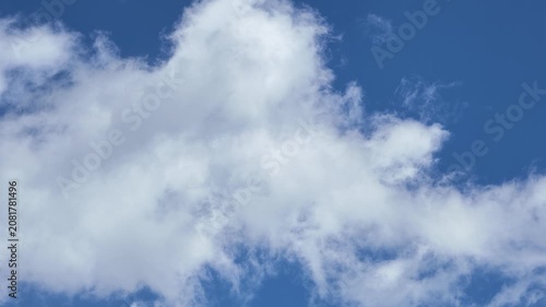 A dynamic sky with fluffy white clouds drifting slowly across a deep, vibrant blue background.