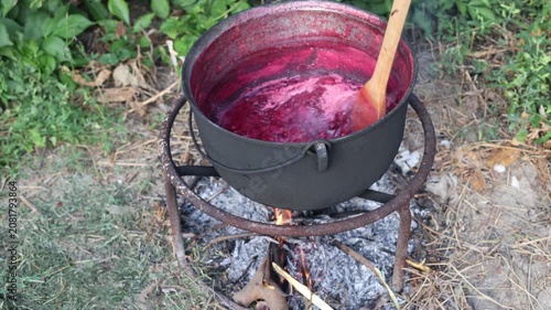 Cooking berry jam in a large cauldron over an open fire outdoors