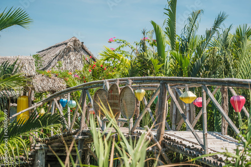 Traditional bamboo footbridge decorated with colorful lanterns in a tropical eco village