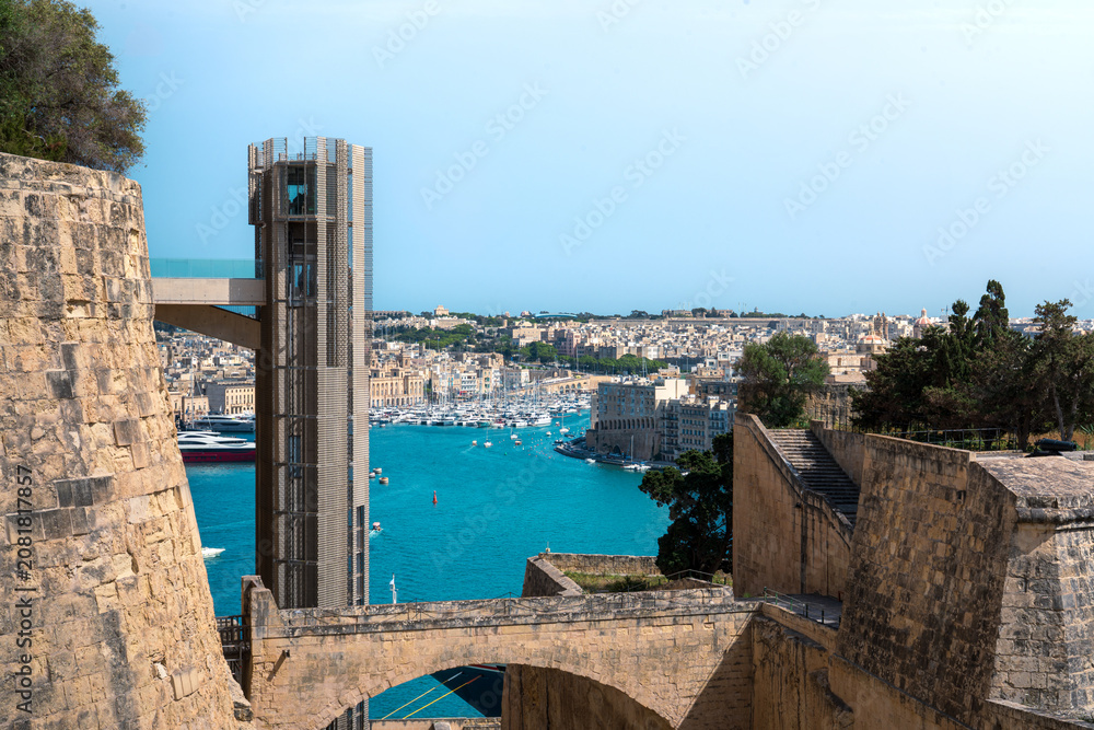 Naklejka premium elevated cityscape view of valletta capital city from malta with clear blue summer skies overhead and limestone old forts either side of shot