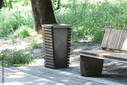 Modern wooden and concrete bench next to litter bin in sunny public park