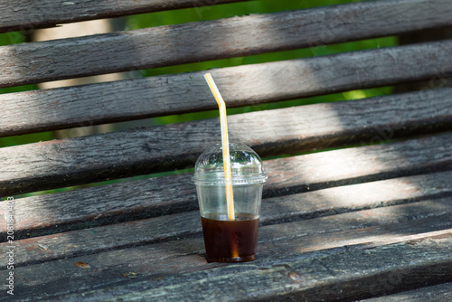 Plastic cup with leftover iced coffee on an old wooden park bench