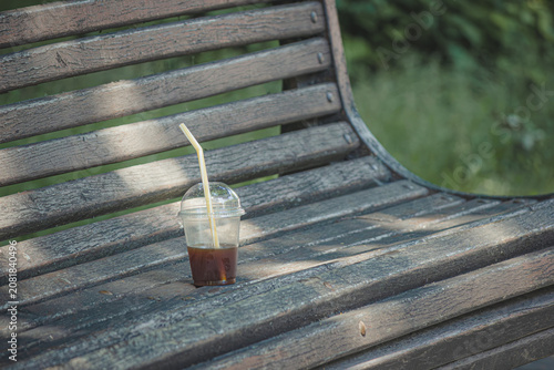 Plastic cup with leftover iced coffee on an old wooden park bench