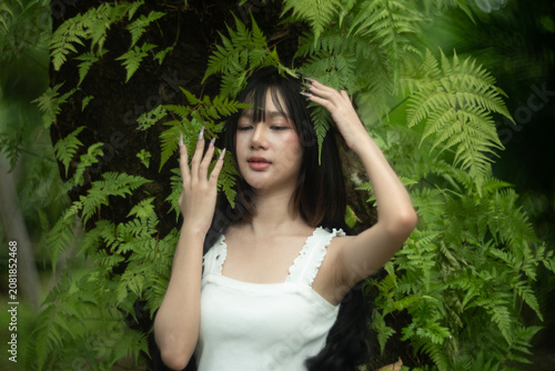 A beautiful young woman among the fern leaves in the forest.