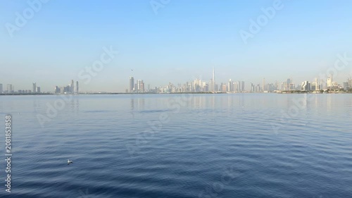 Morning panoramic skyline of Downtown Dubai with Burj Khalifa dominating modern architectural landscape beyond Dubai Creek under clear blue sky