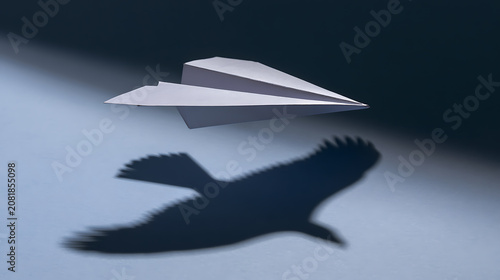 Inspiring white paper airplane with powerful raptor shadow below, symbolizing ambition, freedom, and potential for great achievement and flight