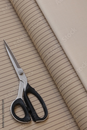 A professional tailor uses sharp shears to cut premium beige pinstripe suiting fabric, creating bespoke luxury apparel in a high-end design atelier.