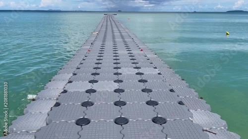 Floating modular pier stretching into calm turquoise water under dramatic clouds in Phuket, Thailand. Scenic tropical seascape with strong leading lines and a peaceful coastal atmosphere