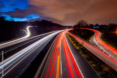 At the Duisburg-Kaiserberg Autobahn junction, two main motorways in the Ruhr Basin (Germany) meet: the A3 and A40. Long exposure with colourful light trails in the evening twilight with dramatic sky.