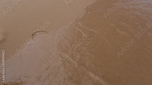 Waves wash away a heart drawing on the sand, a concept of love and romance