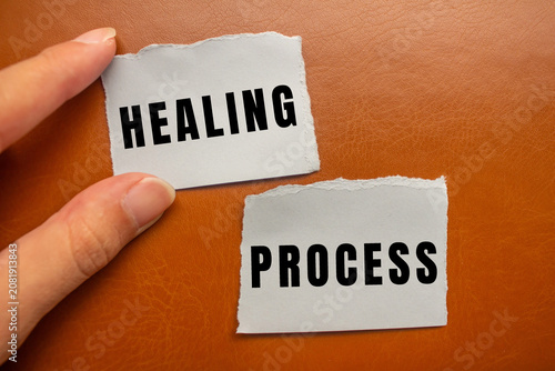 Fotografia Hand holding two pieces of torn paper with the words healing and process on a br