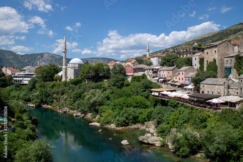 MOSTAR, BOSNIA AND HERZEGOVINA - JUNE 26, 2022: Scenic panoramic view of the historic Koski Mehmed Pasha Mosque and the emerald Neretva River flowing through the old town center of Mostar.