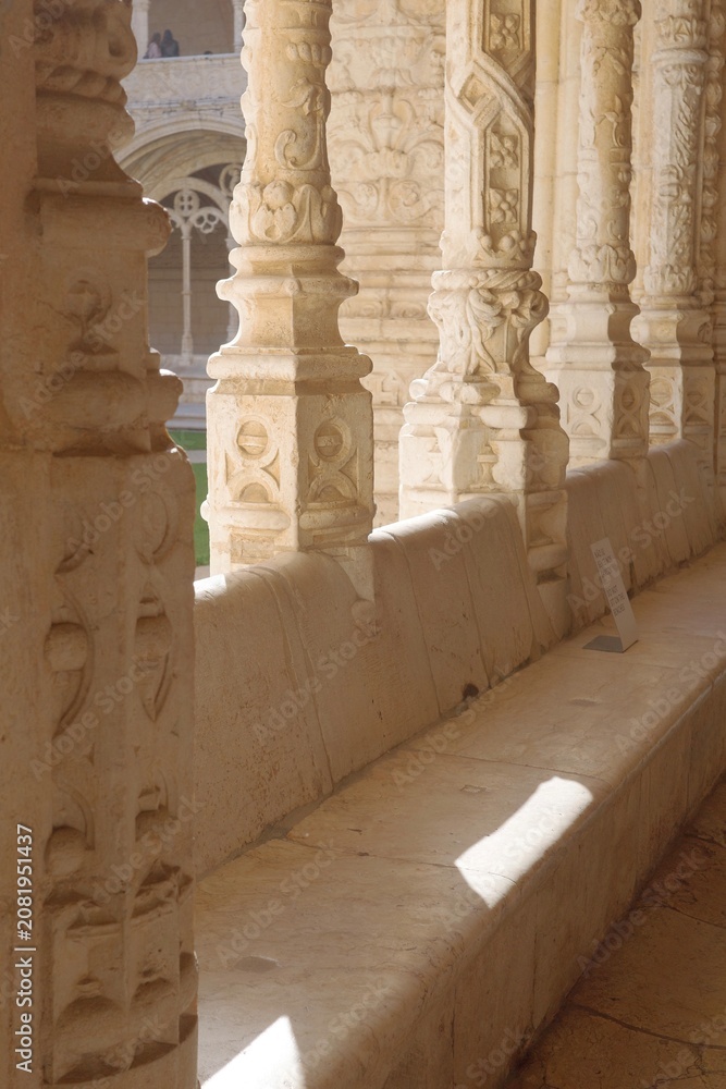 Obraz premium Jerónimos Monastery cloister arcade with twisted stone columns, carved bench and distant visitors, Lisbon, Portugal