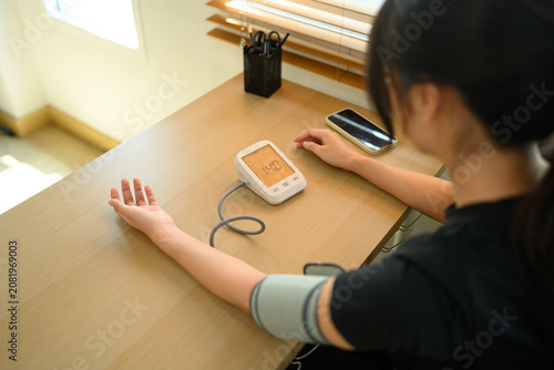Foto Young Asian Woman Measuring Blood Pressure at Home with Digital Sphygmomanometer