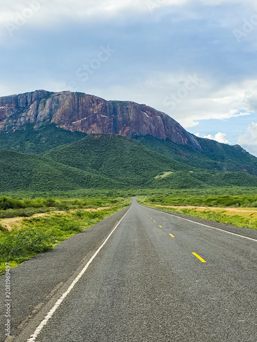 Long straight road traversing Kenyan savanna with mountains
