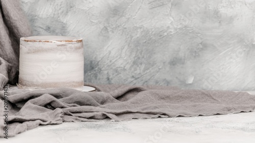 Minimalist white cake on rustic textured background with draped fabric.