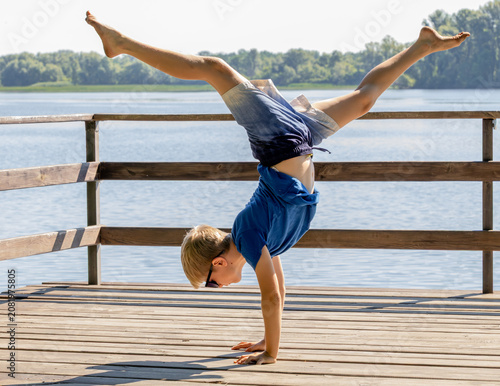 Konstfotografi Athletic little boy doing a handstand on a wooden pier by the river