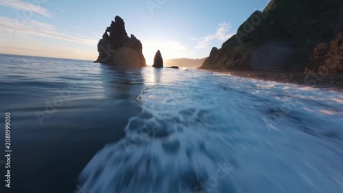 FPV Drone Flight Skimming Ocean Waves Toward Sea Stack at Sunset
