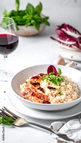 Creamy risotto dish with crispy topping and red wine served on a white table