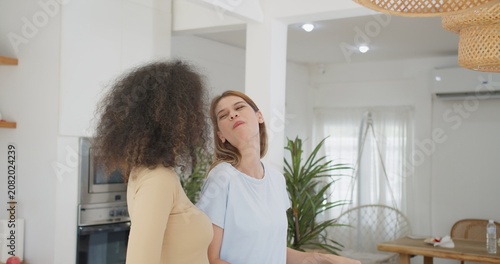 Fotografie Two diverse female friends share a joyful conversation in their modern apartment kitchen, unwinding and bonding while enjoying a happy moment of connection at home