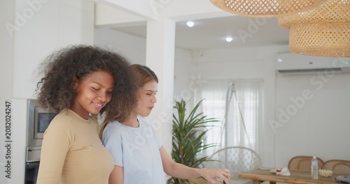 Obraz na plátně Two diverse female friends share a joyful conversation in their modern apartment kitchen, unwinding and bonding while enjoying a happy moment of connection at home