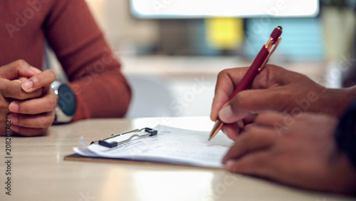 Canvas Print Two people sit at a table, one signing a document