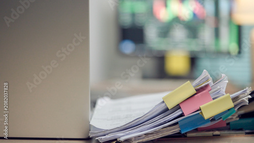 Photos Stacked papers pinned with colorful clips sit beside a laptop