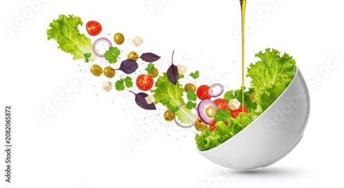 Fresh salad vegetables falling into a white bowl with olive oil pouring down