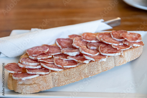 Vielha, Spain. Close up of a traditional breakfast toast topped with slices of cured fuet sausage and extra virgin olive oil, served on a white plate with a napkin inside a local restaurant