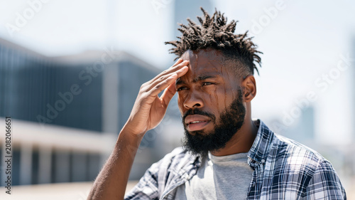 Young african american man experiencing extreme heat and discomfort, feeling exhausted and dehydrated during a summer heatwave in the city outdoors