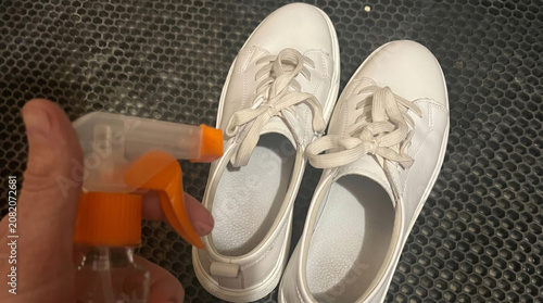 Man spraying cleaner on white sneakers on textured surface  