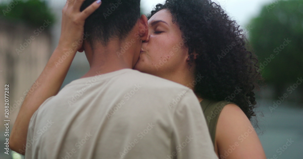 Fototapeta premium Mother embracing her teenage son with a joyful smile and kissing him on the cheek, sharing a tender moment of affection and deep familial bond in a serene outdoor setting