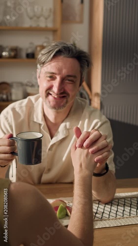 Vertical shot of middle aged Caucasian man holding hands with Caucasian woman and drinking coffee. Ideal for family lifestyle marketing, relationship counseling apps, or insurance commercials