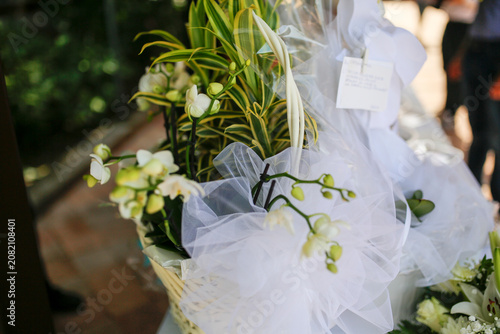 A delicate arrangement of white orchids, green foliage, and soft tulle in a basket, perfect for celebrations or floral decor, bathed in natural light.