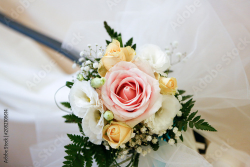 Close-up of a delicate bridal bouquet featuring a soft pink rose, yellow roses, white flowers, and green foliage on a light background.