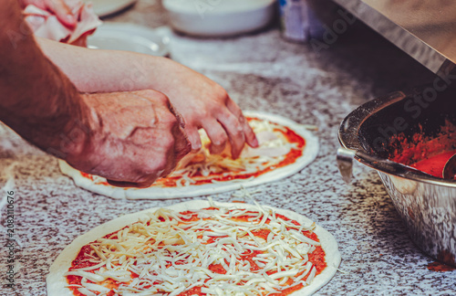 Restaurant kitchen staff preparing fresh pizzas by hand with tomato sauce and mozzarella cheese on a professional countertop. Authentic teamwork and real food preparation in a busy pizzeria.