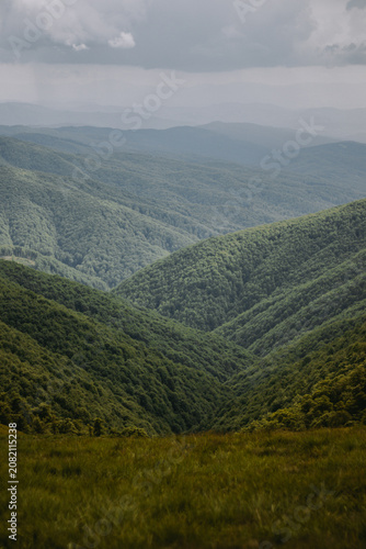 Dramatic panoramic view of Carpathian mountains with layered green hills, forest and valley under stormy sky. Moody landscape capturing the wild and majestic natural beauty of Eastern European nature.