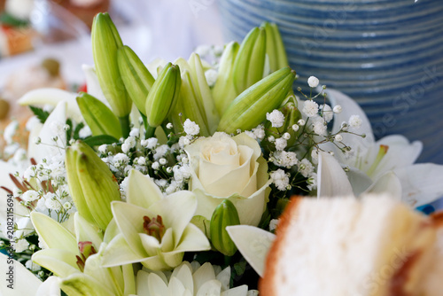 A close-up of a floral arrangement with white lilies, gypsophila, and a central white rose, set against a soft, vibrant backdrop of blurred blue textures.