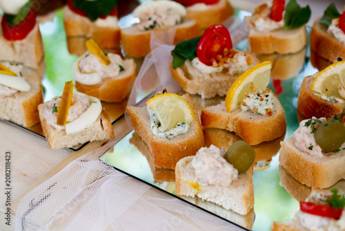 A tray of delicious canapes featuring fresh vegetables, lemon slices, cream toppings, and herbs arranged on reflective mirrors in a bright setting.